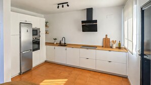 Una cocina moderna con armarios blancos, un refrigerador de acero inoxidable, un microondas, un fregadero y una encimera de madera.