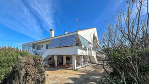 Una casa moderna de dos pisos con techo plano, paneles solares y un patio cubierto.