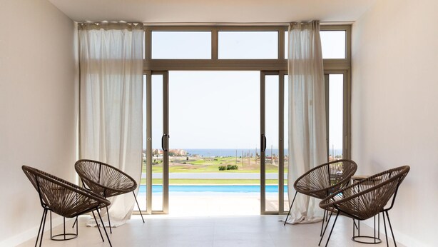 Ein Zimmer mit einer großen SchiebeglasTür, die zu einem Pool führt, zwei Korbsesseln und Blick auf einen Golfplatz.