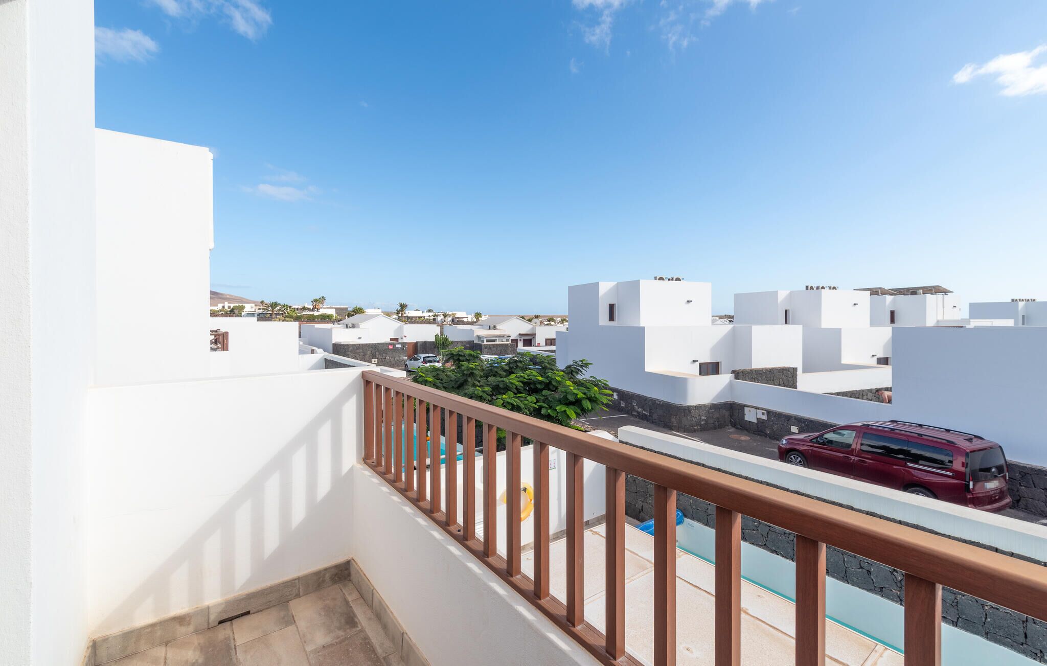 Un balcone con vista su una zona residenziale, un veicolo rosso e un cielo azzurro limpido.