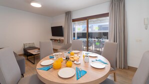 Ein Essbereich mit einem runden Tisch, gedeckt für ein Frühstück, einem Fernseher an der Wand und Blick auf die Terrasse.