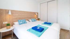 Ein Hotelzimmer mit zwei Betten, einem Holzkopfende, Nachttischlampen, einem kleinen Tisch mit einer Pflanze und einem großen Fenster.
