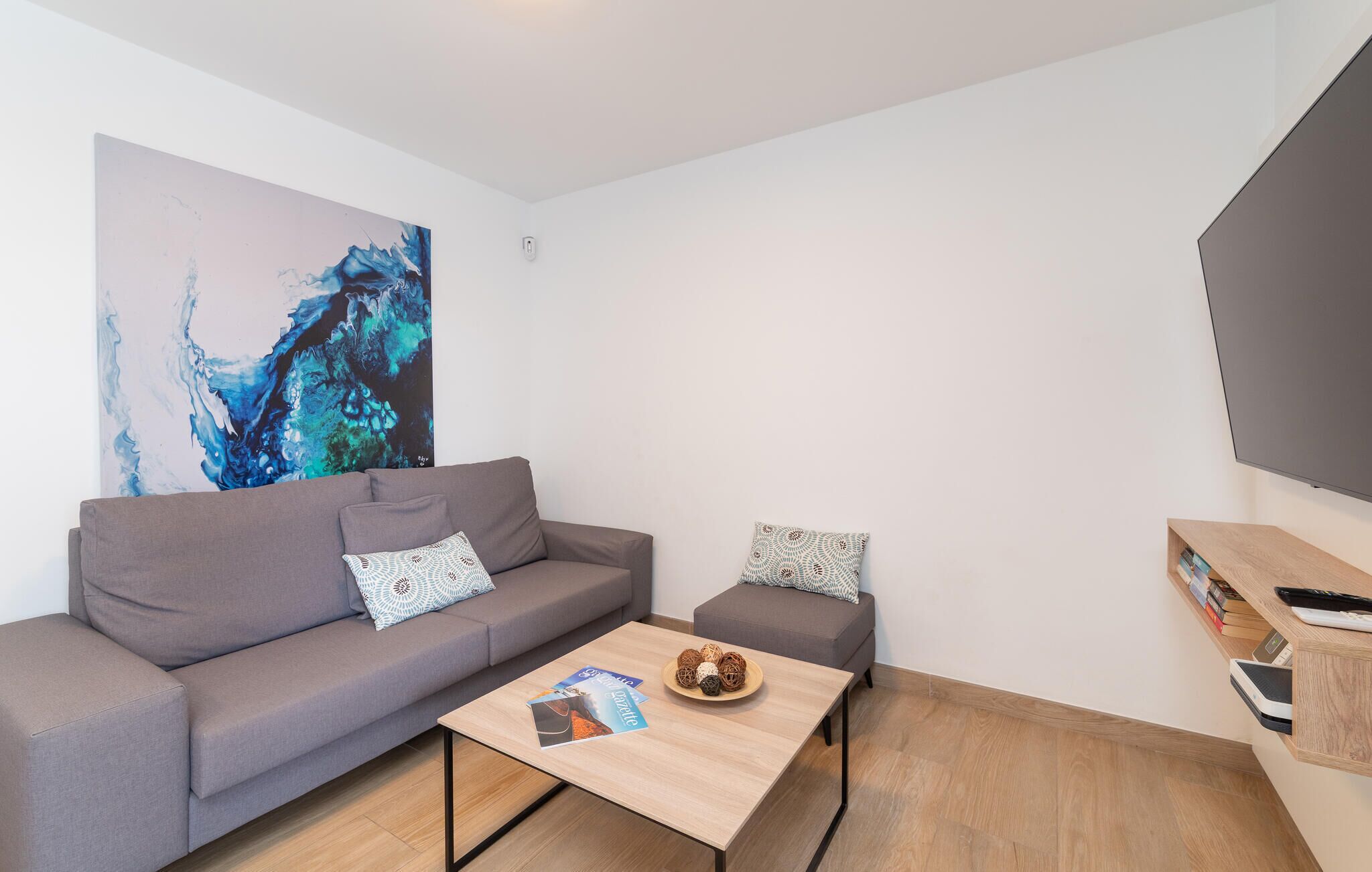 Een moderne woonkamer met een grijze bank, een bijzettafeltje en een schilderij aan de muur.