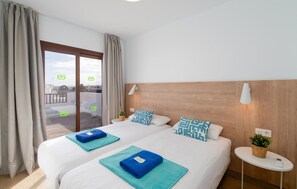 A hotel room with two beds, a balcony, a wooden headboard, a small side table, and a wall-mounted lamp. - Nice home in Lanzarote with private swimming pool, can be inside or outside (Lanzarote)