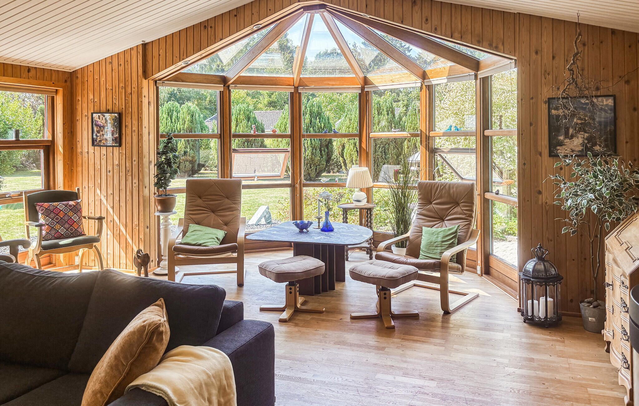 Una habitación acogedora con paredes de madera, ventanas amplias, una mesa redonda y asientos cómodos.