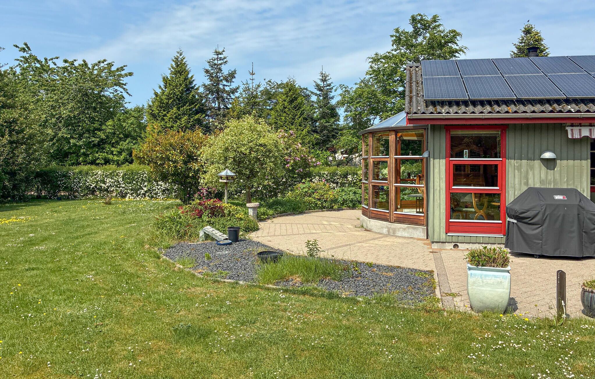 Una casa con jardín, zona de barbacoa y panel solar en el techo.