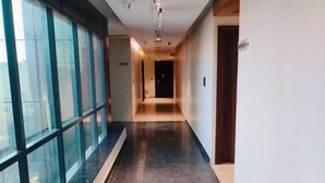 A long, narrow hallway with a polished floor, large windows on one side, and a door at the end. - Hotel Raaj Palace (Agra)
