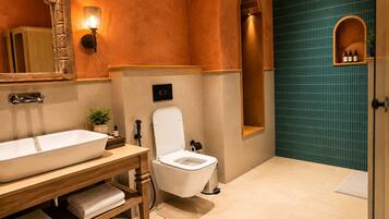 Een badkamer met een groot wit wastafel, toilet, spiegel en een wandplank met flessen.