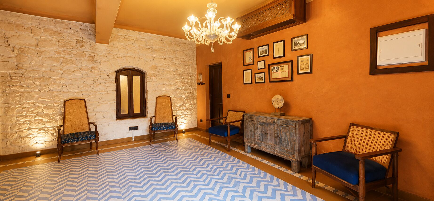 A room with a stone wall, wooden chairs, a patterned floor, and framed pictures on the wall.