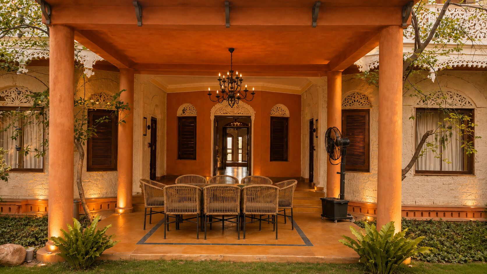 A covered outdoor dining area with a table and chairs, a chandelier, and a fan.