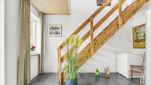 A room with a wooden staircase, a potted plant, a radiator, and a framed picture on the wall.
