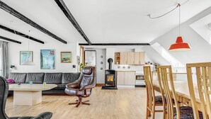 A modern loft with exposed beams, a central fireplace, a dining area, and a kitchen with wooden cabinets.