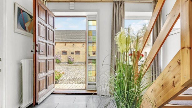 An open door leading to a courtyard with a tiled floor, a potted plant, and a wooden staircase.