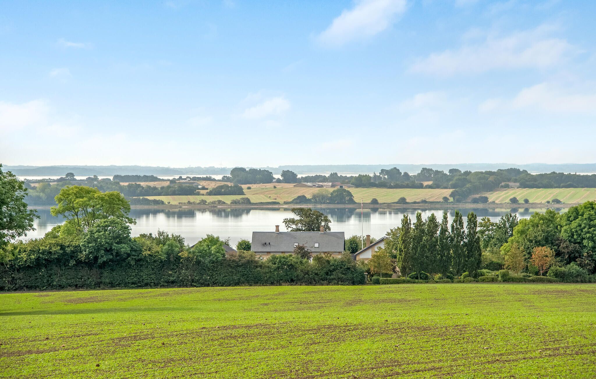 A rural landscape with a lake, fields, and a house.