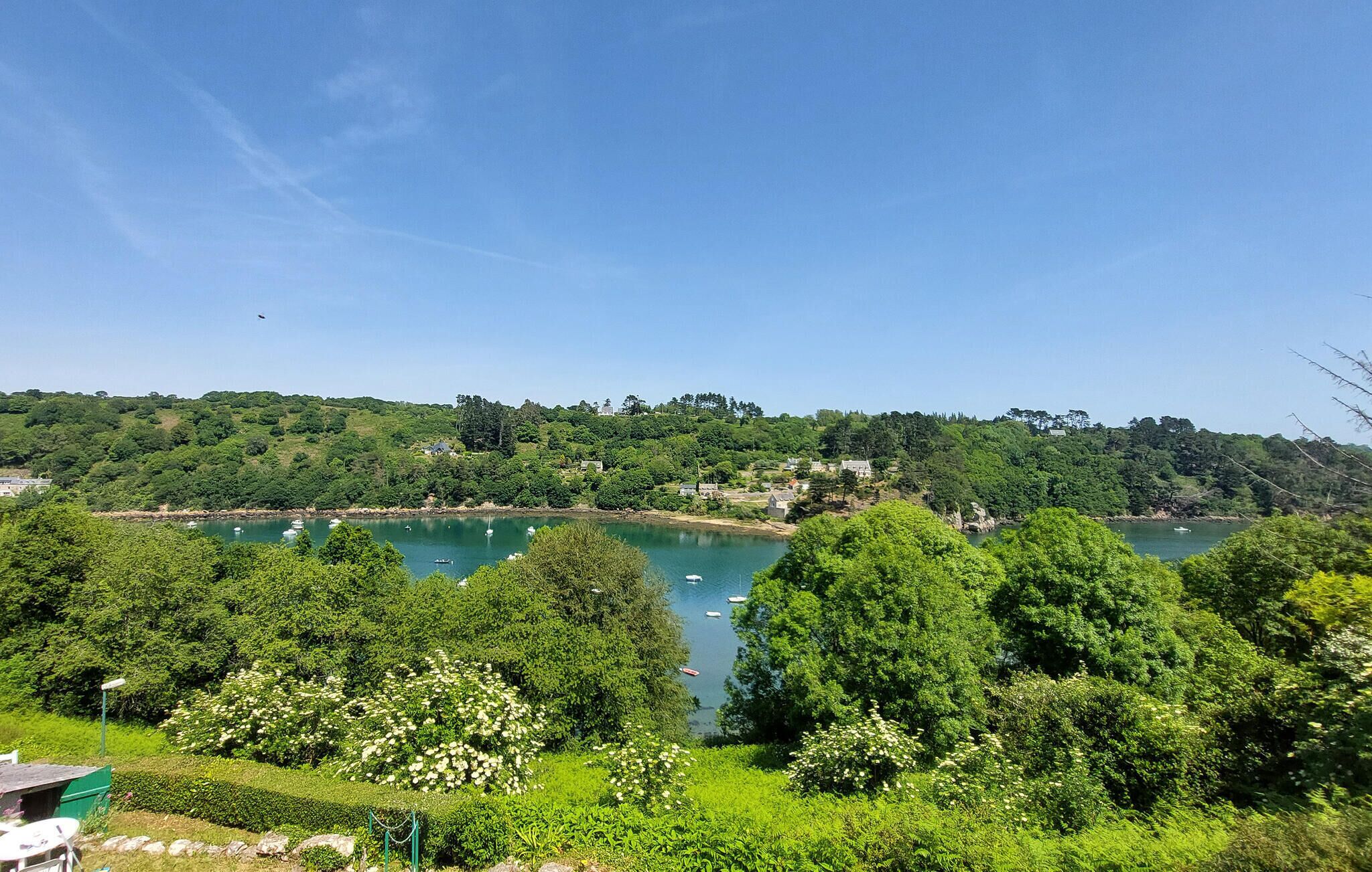Un paysage côtier avec une étendue d’eau, des arbres et des bâtiments visibles au loin.