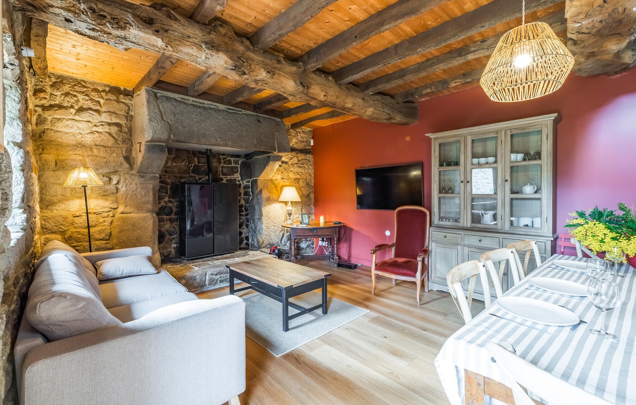 A rustic interior with stone walls, a fireplace, a sofa, a dining table set, and a red accent wall.