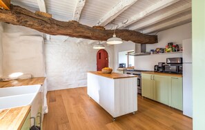 A kitchen with a central island, wooden flooring, white cabinetry, and a rustic ceiling beam. - Stunning home in Ploumillau with WiFi (Ploumillau)