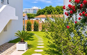 Ein Garten mit einem Pfad, einer Palme und einem Strauch mit roten Blüten.