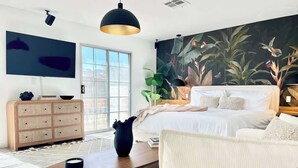 A modern bedroom with a large bed, a flat-screen TV, a large window, and a tropical-themed mural. - LUX 6BR/3BA Stylish House w/piano, bar, pool&spa (Las Vegas)