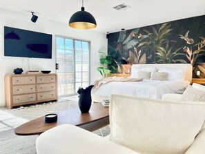 Ein modernes Schlafzimmer mit einem großen Bett, einem Flachbildfernseher, einem großen Fenster und einem Wandbild im tropischen Stil.