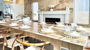 A dining room with a long table set for a meal, a fireplace, and wicker pendant lights. - LUX 6BR/3BA Stylish House w/piano, bar, pool&spa (Las Vegas)
