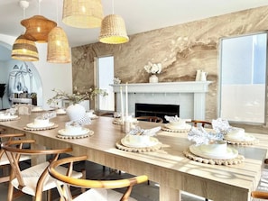 Ein Esszimmer mit einem langen Tisch, der für eine Mahlzeit gedeckt ist, einem Kamin und Korbschirme.