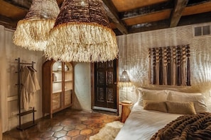 Ein Schlafzimmer mit Steinboden, einem Bett mit weißer Tagesdecke, einem Holzschrank und einer hängenden Leuchte.