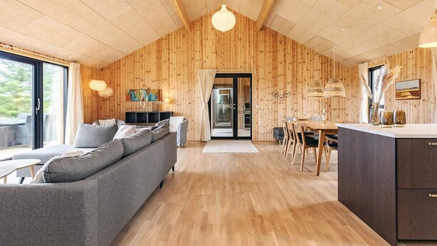 A modern interior with a wooden ceiling, a grey sofa, a dining area, and a kitchen. - 5 Star Holiday Home in Saltum (Saltum)