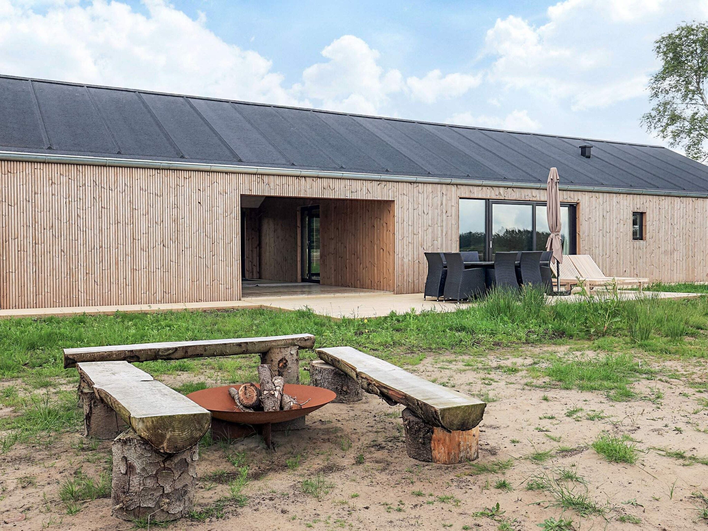 Un bâtiment moderne avec une façade en bois, un espace extérieur aménagé avec des sièges et un foyer.