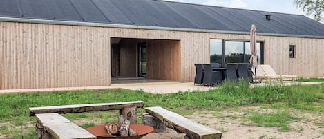 A modern building with a wooden exterior, a covered outdoor seating area, and a fire pit.