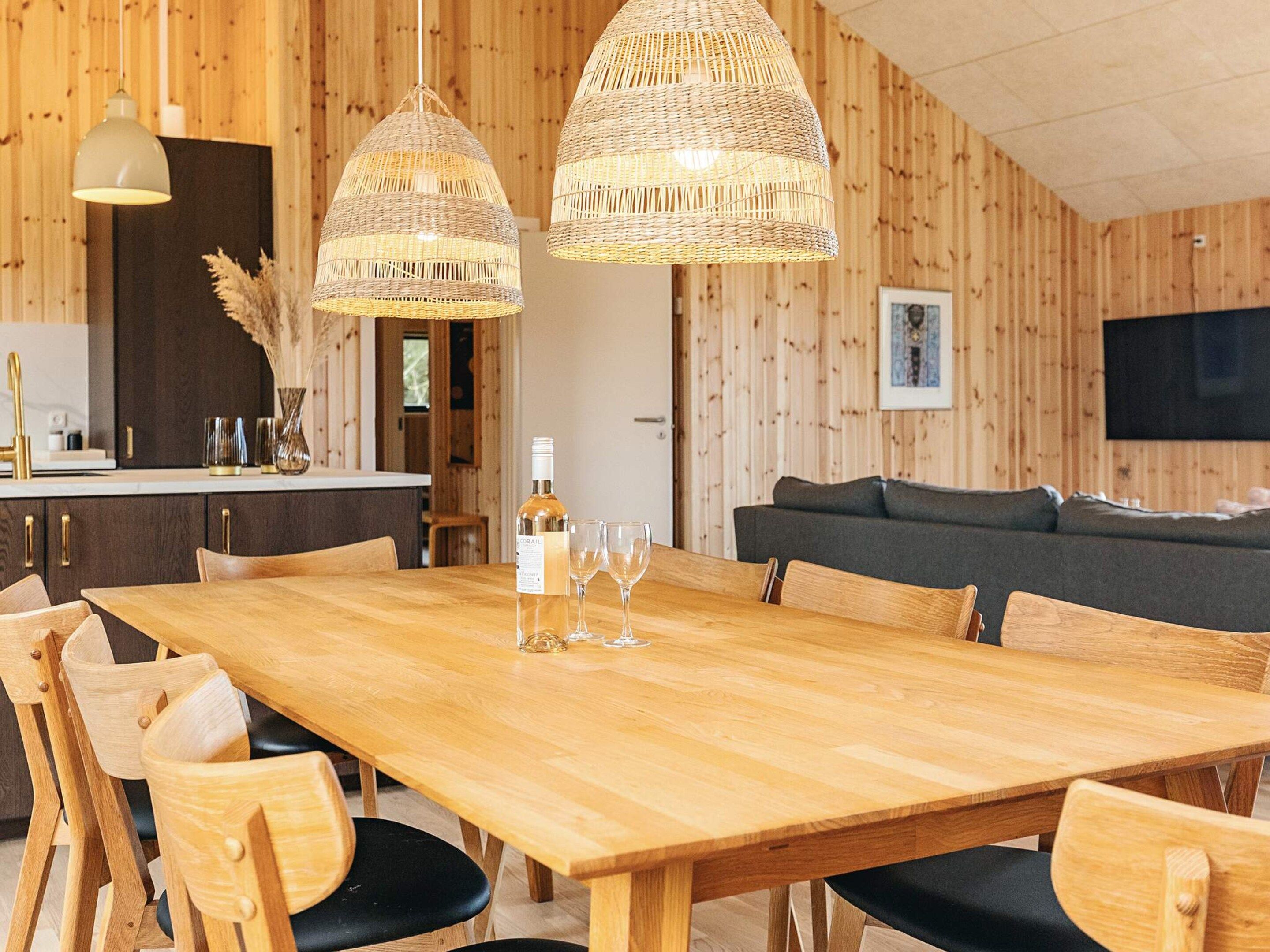Un intérieur en bois comprenant une table à manger, des chaises, un canapé et des lampes en osier suspendues.