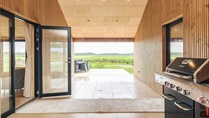 A modern kitchen with a built-in grill, a sliding glass door leading to a patio with outdoor seating, and a view of the countryside. - 5 Star Holiday Home in Saltum (Saltum)