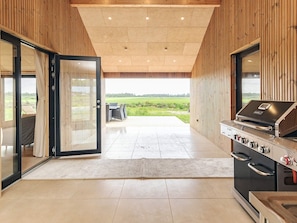 Et moderne køkken med indbygget grill, en skydedør til en terrasse med udendørs møbler, og udsigt over landskabet.