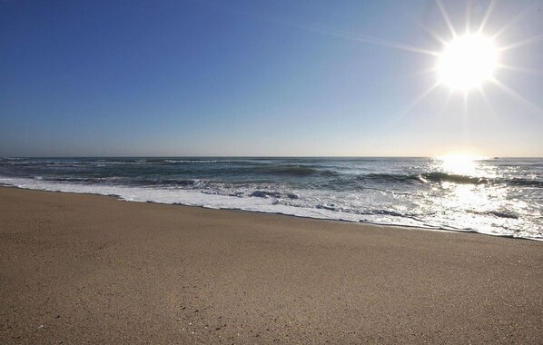 Ein Strand mit Wellen, wolkenlosem Himmel und strahlender Sonne.