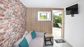 A room with a brick wall, a sofa with cushions, a small table, a TV mounted on the wall, and a door leading outside. - 2 bedroom awesome home in Perpignan (Perpignan)