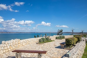 Ein mit Steinen gepflasterter Außenbereich mit einer Bank, einer Steinmauer und Blick auf das Meer.