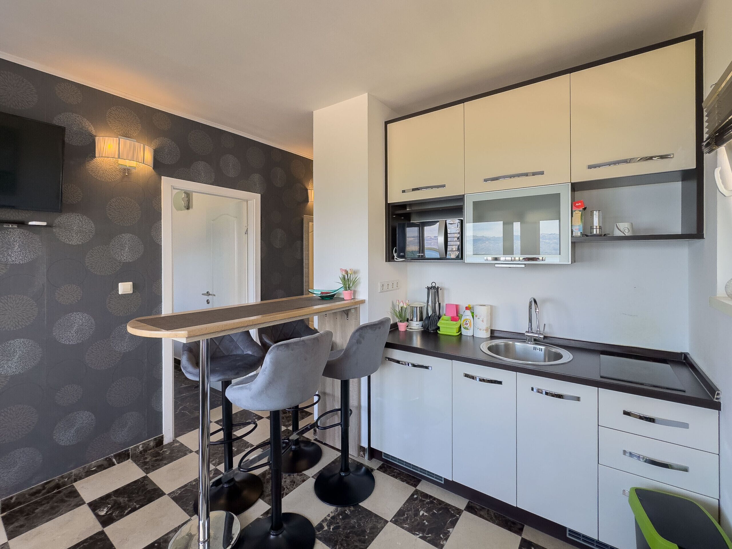 A modern kitchen with a bar area, white cabinets, and a checkered floor.
