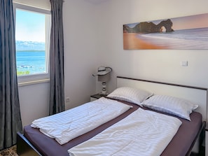 Ein Hotelzimmer mit Bett, einem Meereslandschaftsbild, einem Fenster mit Vorhängen und Blick aufs Meer.