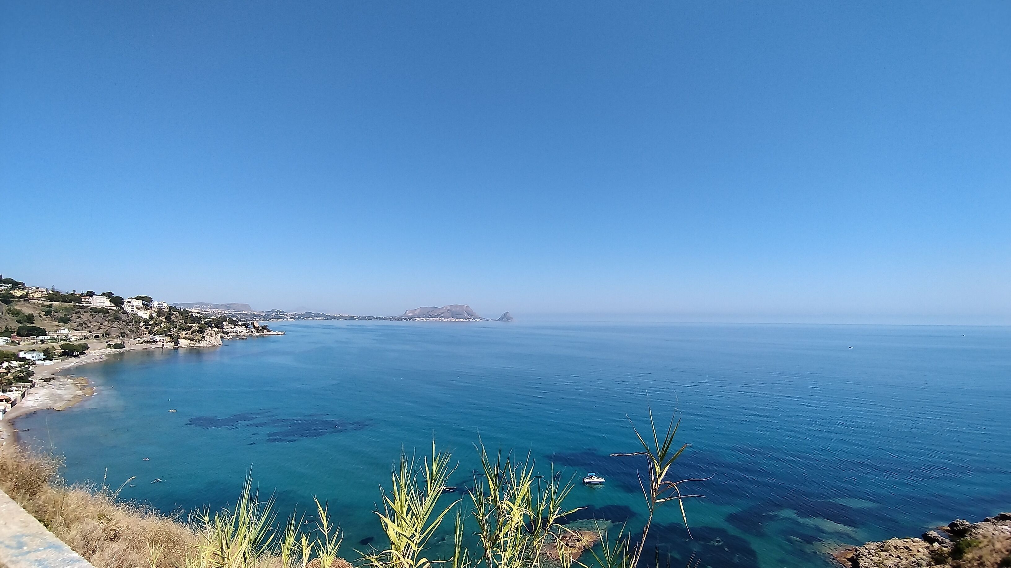 Un paysage côtier caractérisé par une eau d’un bleu limpide, un terrain rocheux et des collines qui se dessinent à l’horizon.