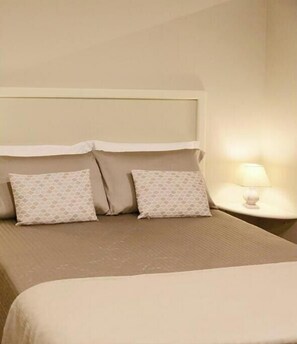 Ein Hotelzimmer mit einem Bett, zwei gemusterten Kissen, einem Nachttisch mit Lampe und einem Kopfteil.