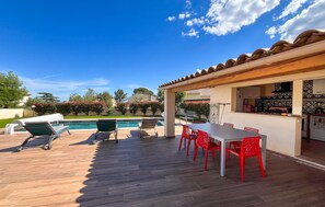 Eine Terrasse mit Pool, Sitzgelegenheiten im Freien und einer Küchenzeile.