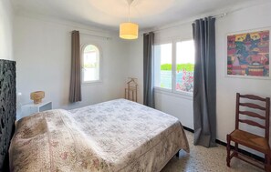 Ein Schlafzimmer mit einem Bett, einer Hängelampe, einem Fenster und einem Sessel.
