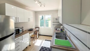 Una cucina moderna con mobili bianchi, un frigorifero in acciaio inossidabile, forno integrato, macchina da caffè e una finestra con vista esterna.