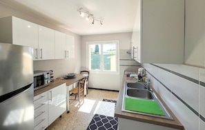 Eine moderne Küche mit weißen Schränken, einem Edelstahl-Kühlschrank, einem eingebauten Backofen, einer Kaffeemaschine und einem Fenster mit Blick nach draußen.