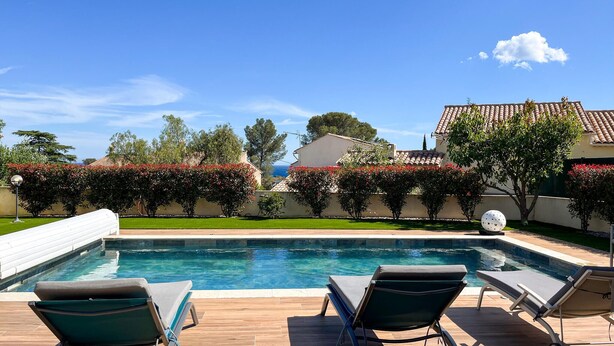 Una piscina con lettini, vista libera sul mare e un giardino curato.