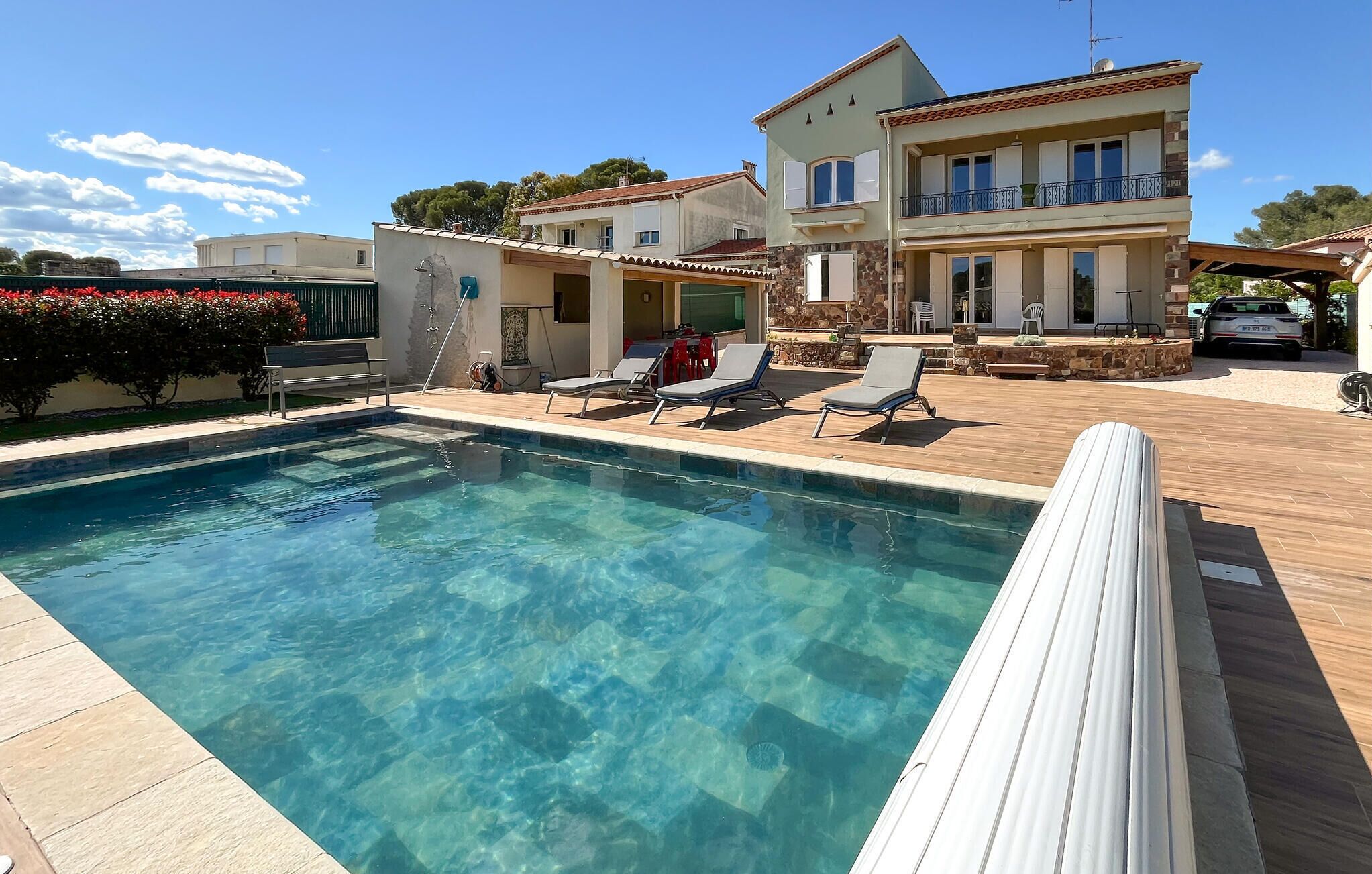 Une piscine avec des chaises longues, une terrasse couverte et un immeuble à plusieurs étages doté de balcons.