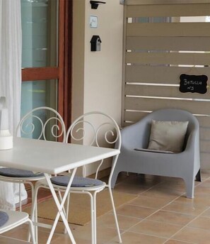 A dining area with a white table and chairs, a grey cushioned chair, a window with curtains, and a sign reading 'Betulla n°3'. - The Seven Ways - Birch Apartment with Relaxing Porch (Piemonte)