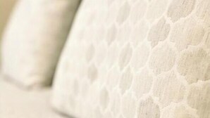 Primer plano de una cama con un cabecero blanco texturizado y almohadas.