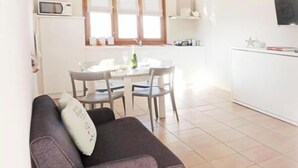 Un espacio habitable compacto con un sofá gris, una mesa de comedor con sillas, una zona de cocina y un televisor montado en la pared.