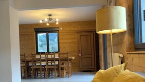 A modern living room with a grey sofa, yellow cushions, a wooden dining table, and chairs. A large window provides a view of the outdoors. - Les Privilèges family home in the heart of nature, 5 minutes from the town center (Gérardmer)